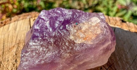 An amethyst crystal sitting on a piece of wood in color