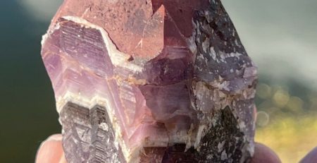 A person holding a piece of purple amethyst in front of a lake.