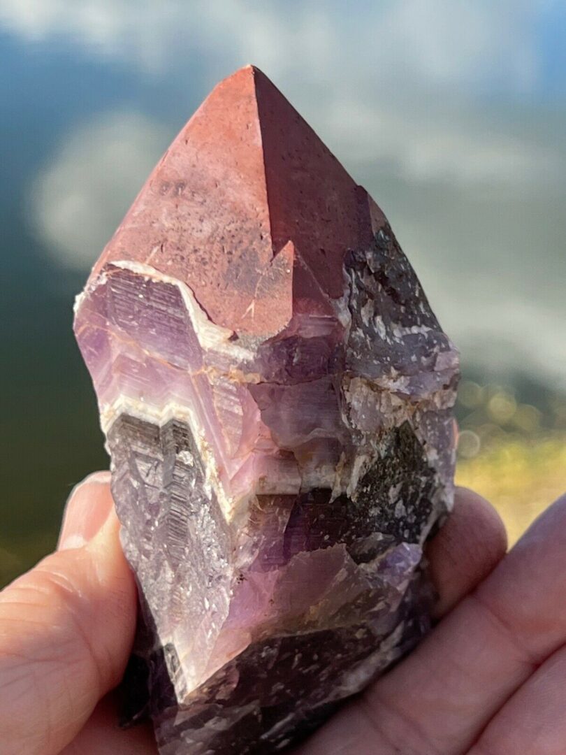 A person holding a piece of purple amethyst in front of a lake.