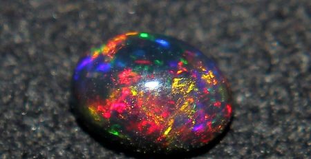 An oval shaped opal sitting on a black surface.