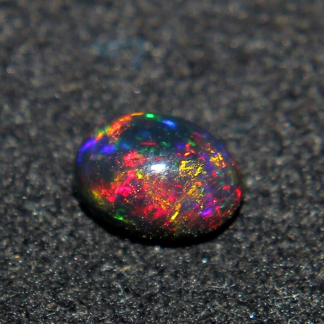 An oval shaped opal sitting on a black surface.