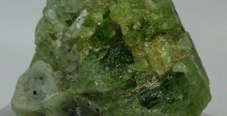 A piece of green quartz sitting on top of a piece of glass.