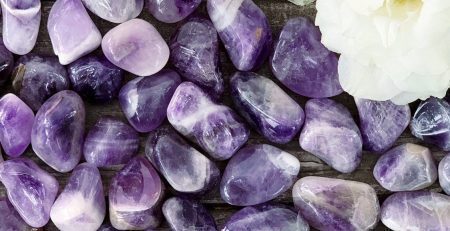 Amethyst pebbles and white flowers on a wooden table.