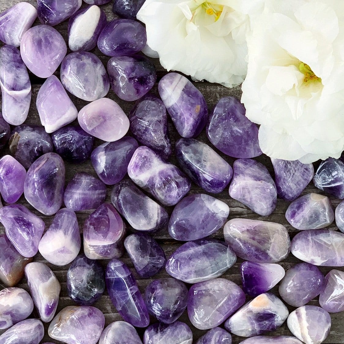 Amethyst pebbles and white flowers on a wooden table.