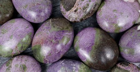 A bunch of purple and green marble eggs on a table.