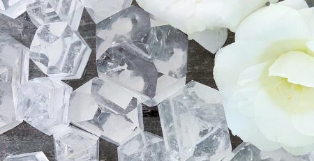 Clear quartz crystals and white roses on a wooden table.