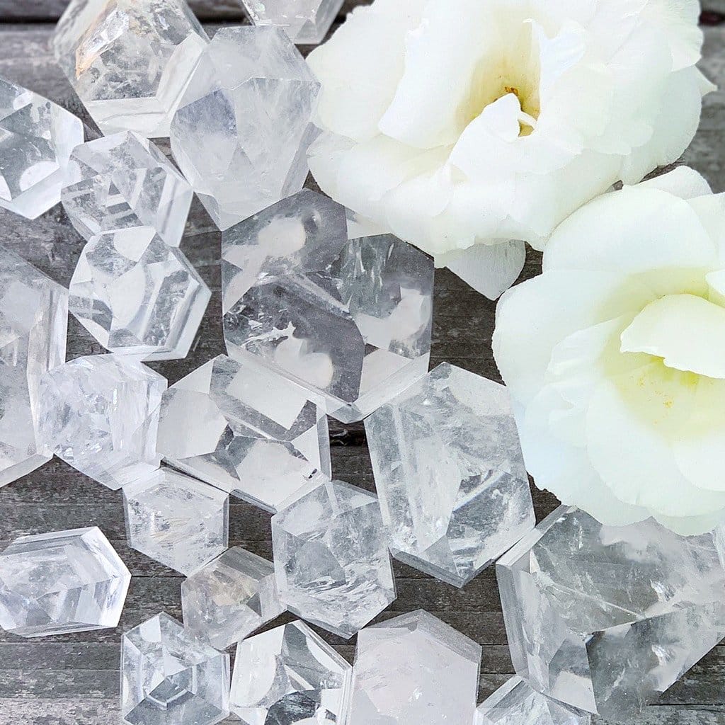 Clear quartz crystals and white roses on a wooden table.