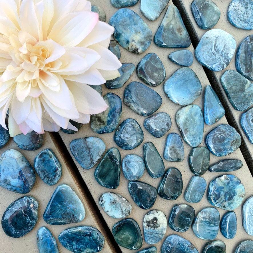 Blue labradorite pebbles on a wooden table with a flower.