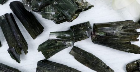 A bunch of black tourmaline crystals on a white surface.