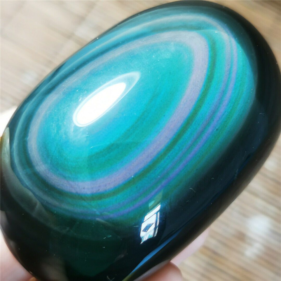 A hand holding a green and blue tiger eye stone.