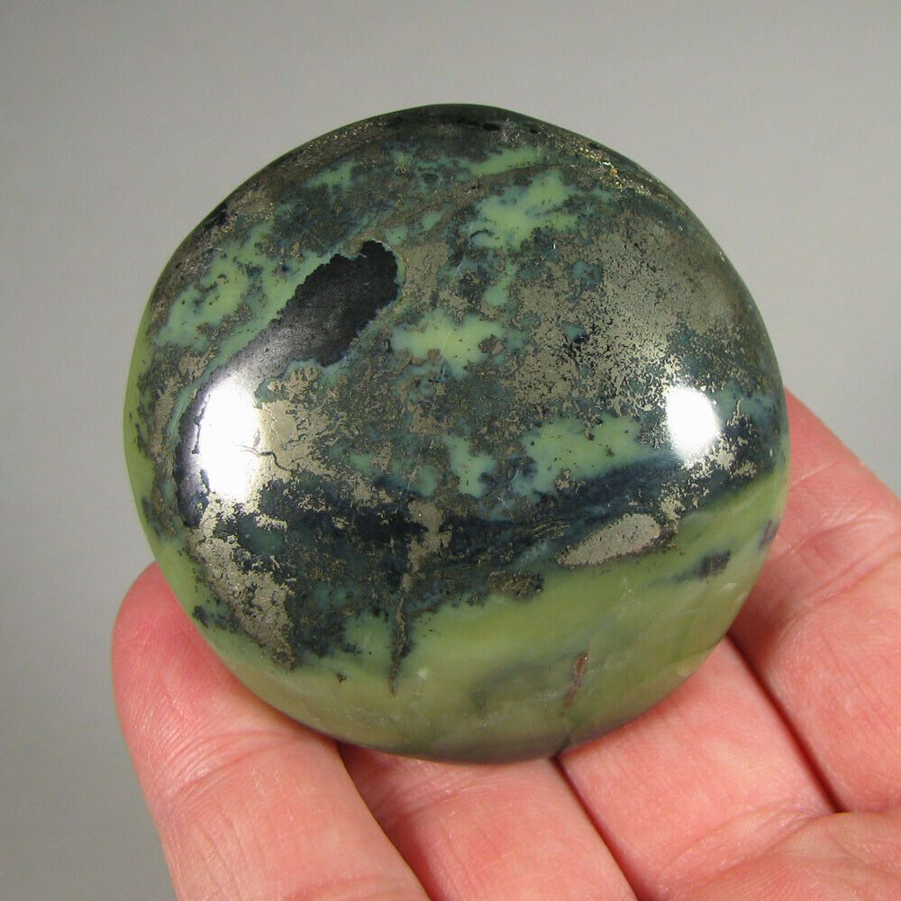 A person holding a green and black stone in their hand.