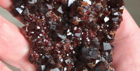 A person holding a piece of red garnet in their hand.