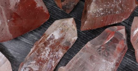 A group of pink and red quartz crystals on a dark surface.