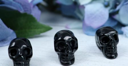 Three black skulls on a table next to flowers.