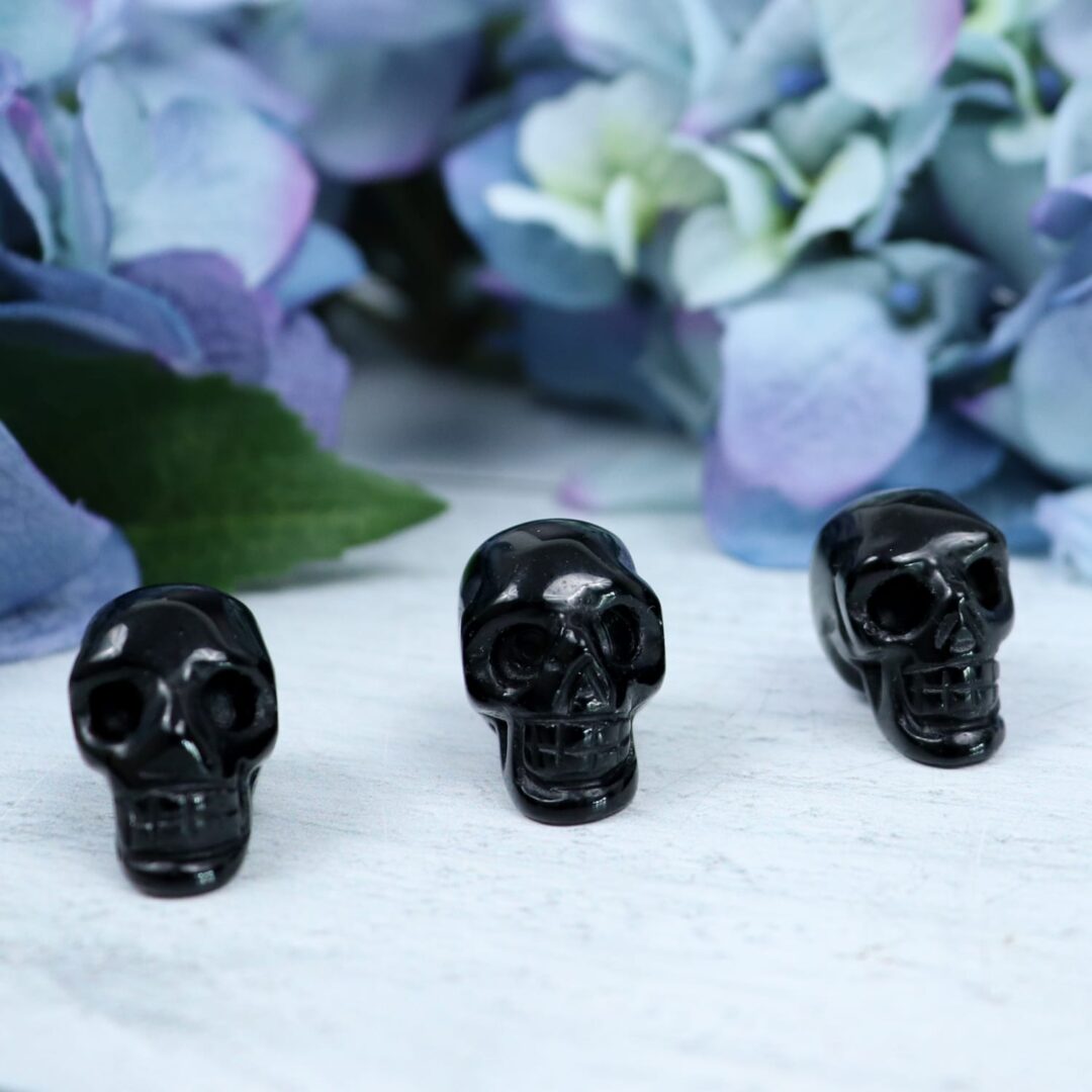 Three black skulls on a table next to flowers.