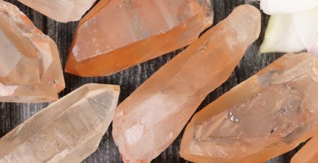 A bunch of orange quartz crystals on a wooden surface.