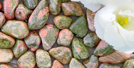 A white flower is placed on a bed of green and pink rocks.