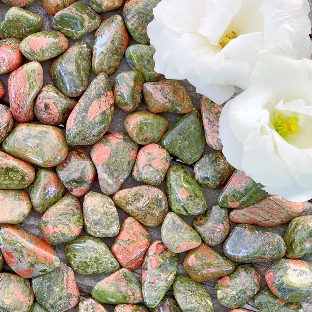 A white flower is placed on a bed of green and pink rocks.