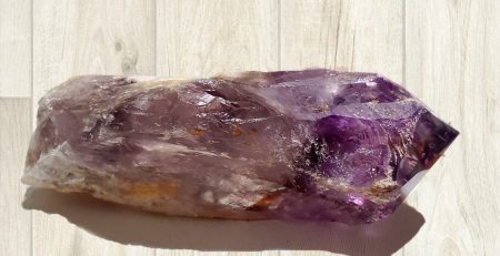 A Bahia Amethyst 7" Dragon Tooth Scepter, deep purple with rainbows on a wooden floor.