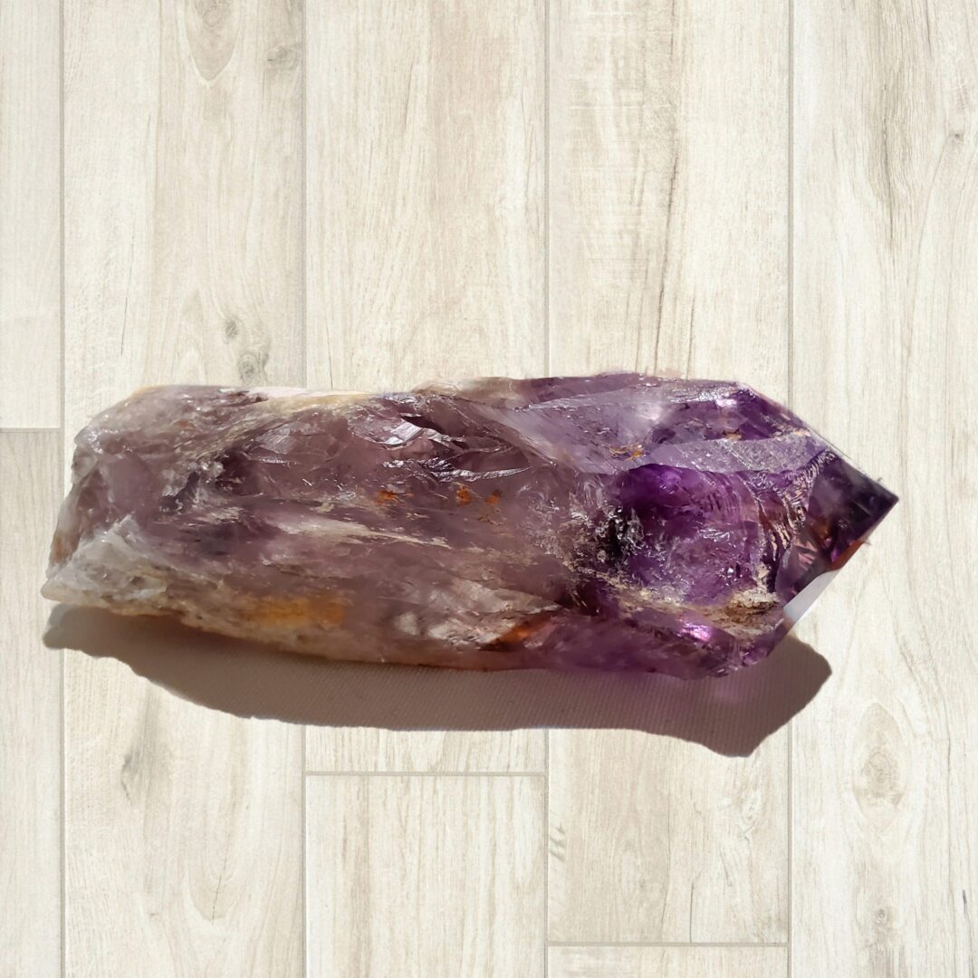 A Bahia Amethyst 7" Dragon Tooth Scepter, deep purple with rainbows on a wooden floor.