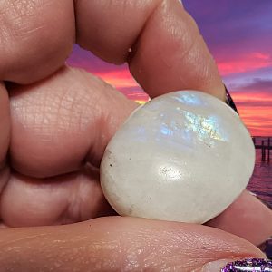 Hand holding a moonstone against a sunset.