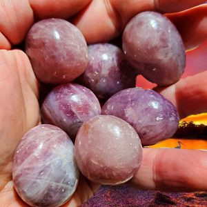 Hand holding six purple amethyst tumbled stones.