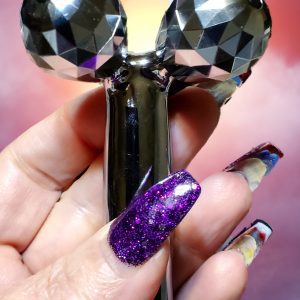 Silver face roller held in hand with purple glitter nails.