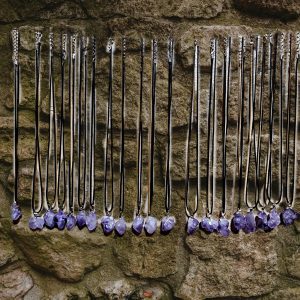 Amethyst necklaces hanging on stone wall.