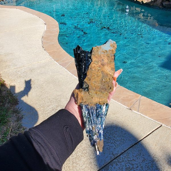 Person holding blue and black crystal by pool.