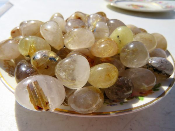 Golden rutilated quartz tumbled stones on plate.
