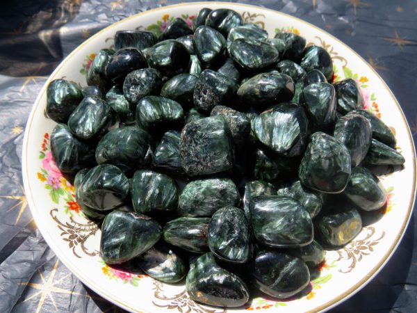 Green and black tumbled gemstones in a bowl.