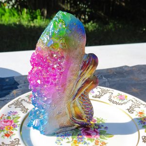 A plate with a Rainbow Angel Aura Mermaid with Rainbow Cluster Quartz figurine on it.