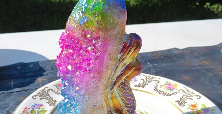 A plate with a Rainbow Angel Aura Mermaid with Rainbow Cluster Quartz figurine on it.