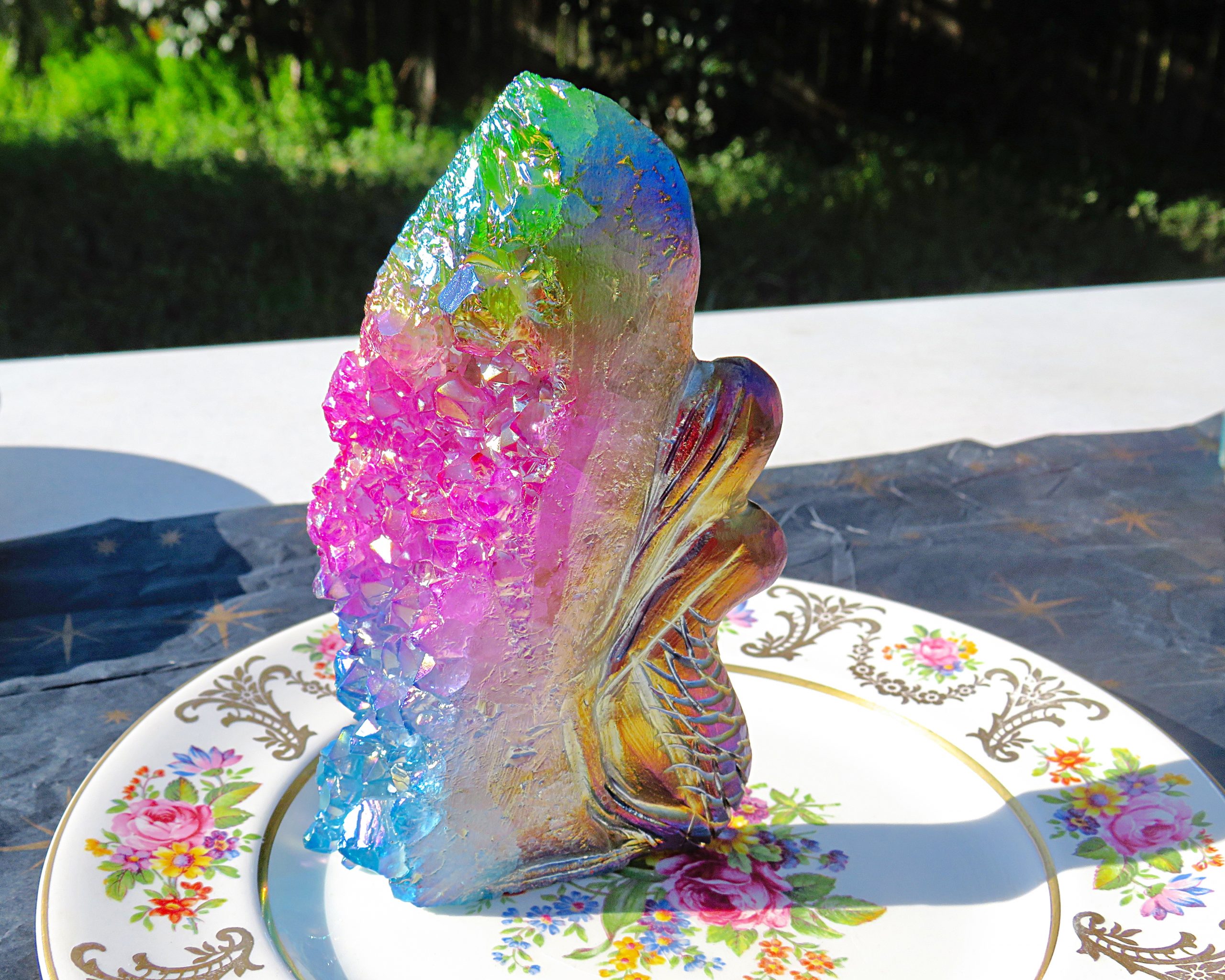 A plate with a Rainbow Angel Aura Mermaid with Rainbow Cluster Quartz figurine on it.