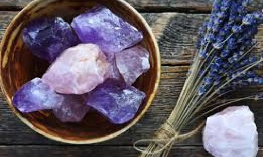 A bowl of crystals and lavender on a wooden wooden table.