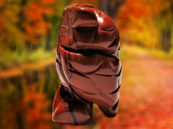 Carved red stone figurine against autumn leaves.