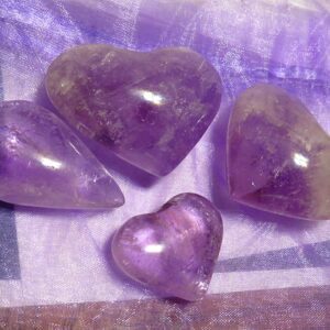 Four heart-shaped amethyst crystals on fabric.