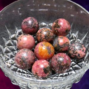 Pink and black gemstone spheres in bowl.