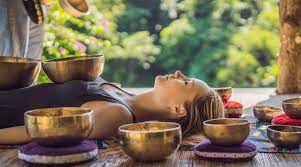 A woman laying on the ground with singing bowls in front of her.